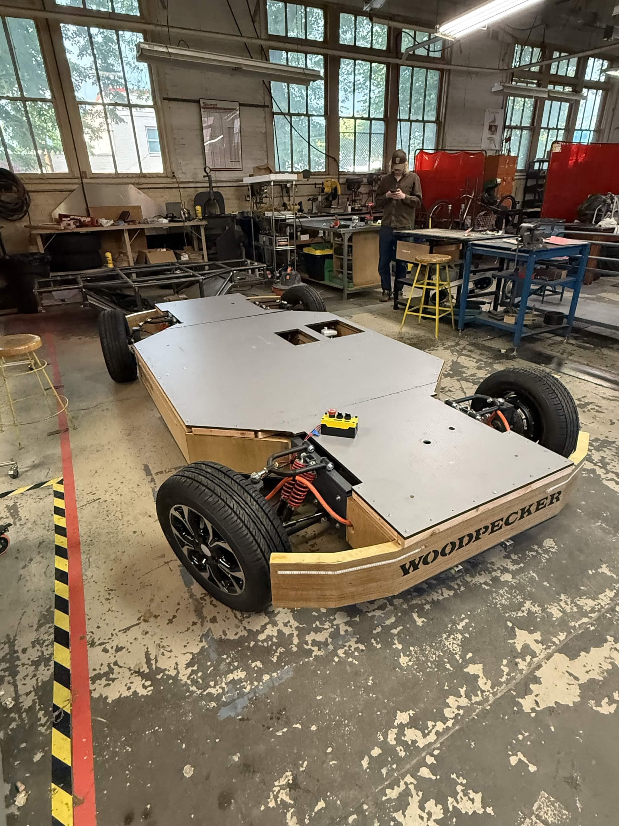 Woodpecker LSEV rolling chassis in the shop: wooden frame, four wheels with suspension and steering installed, gray platform deck on top.